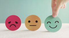 Dieses Bild zeigt eine Hand, die ein grünes Papier-Smiley für eine Feedback-Bewertung auswählt.